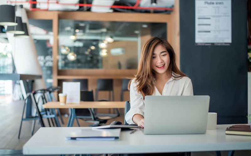 Happy young asian businesswoman sitting on her workplace in the office. Young woman working at laptop in the office. (Happy young asian businesswoman sitting on her workplace in the office. Young woman working at laptop in the office., ASCII, 117 comp